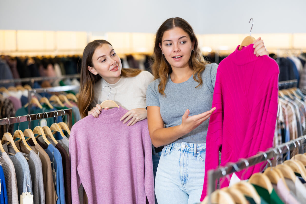 Portrait d'une consultante confiante aidant une fille à choisir un pull en tricot chaud dans un magasin des vêtements de seconde main